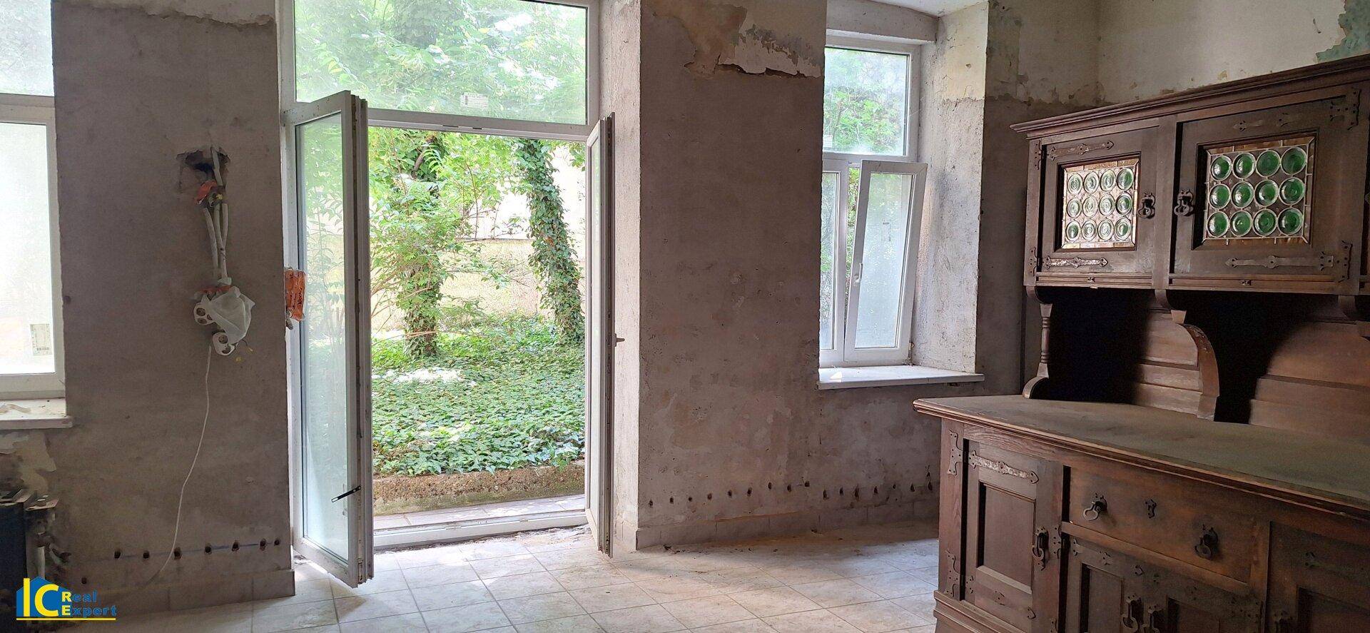 Innenraum mit abgenutzten Wänden, Fliesenboden und direktem Zugang zum Gartenbereich.