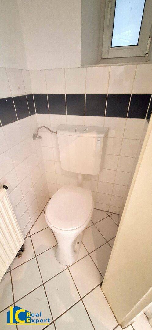 Separate Toilette mit WC, weißen Fliesen und einem Fenster für natürliche Belüftung.