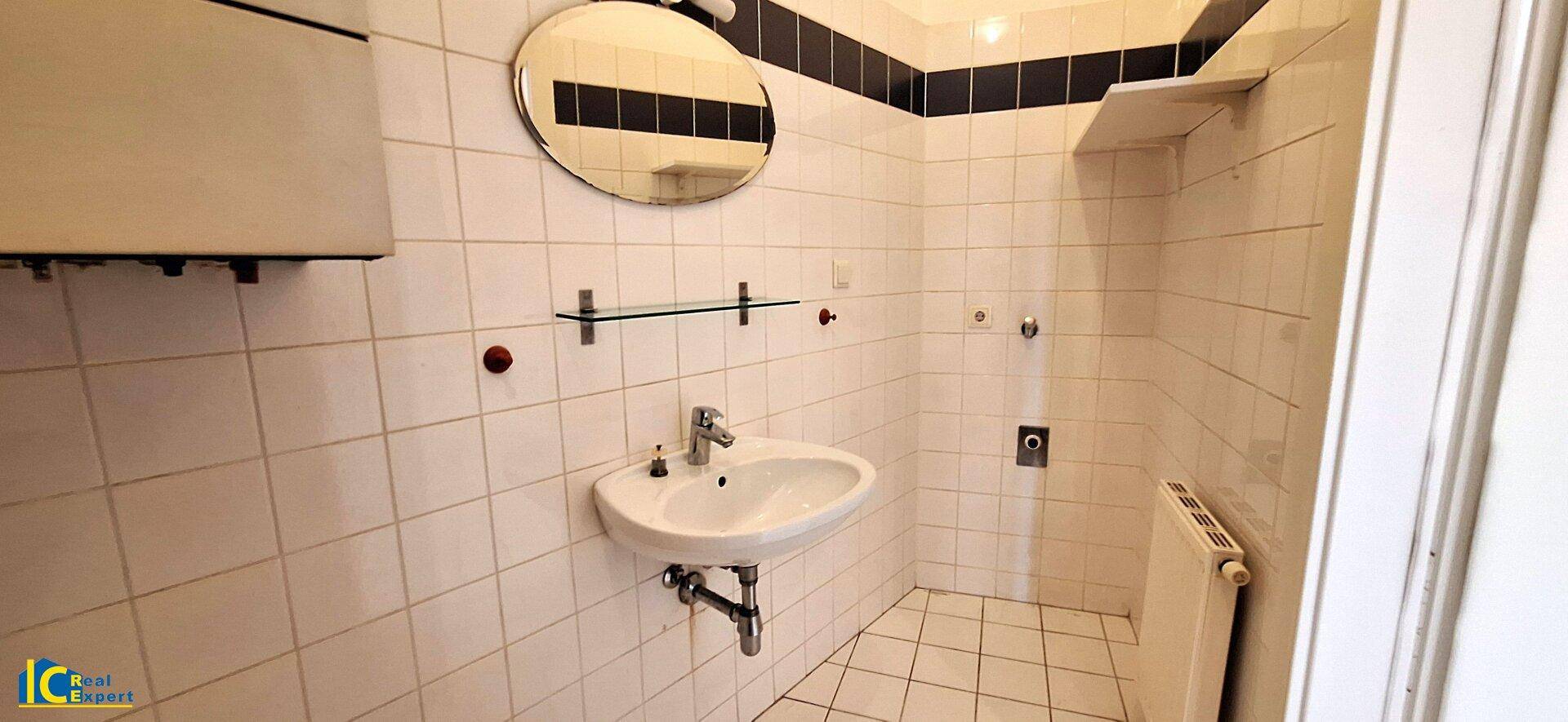Badezimmer mit Waschbecken, rundem Spiegel und weißen Fliesen, ausgestattet mit Heizkörper.
