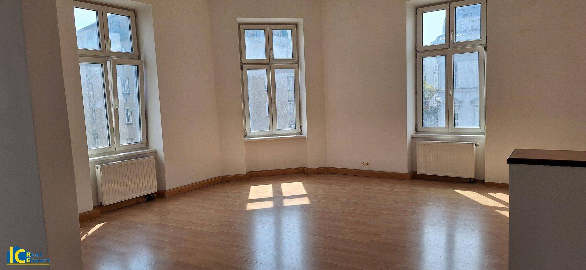Lichtdurchfluteter Raum mit Holzparkett und großen Fenstern, die viel Tageslicht hereinlassen.