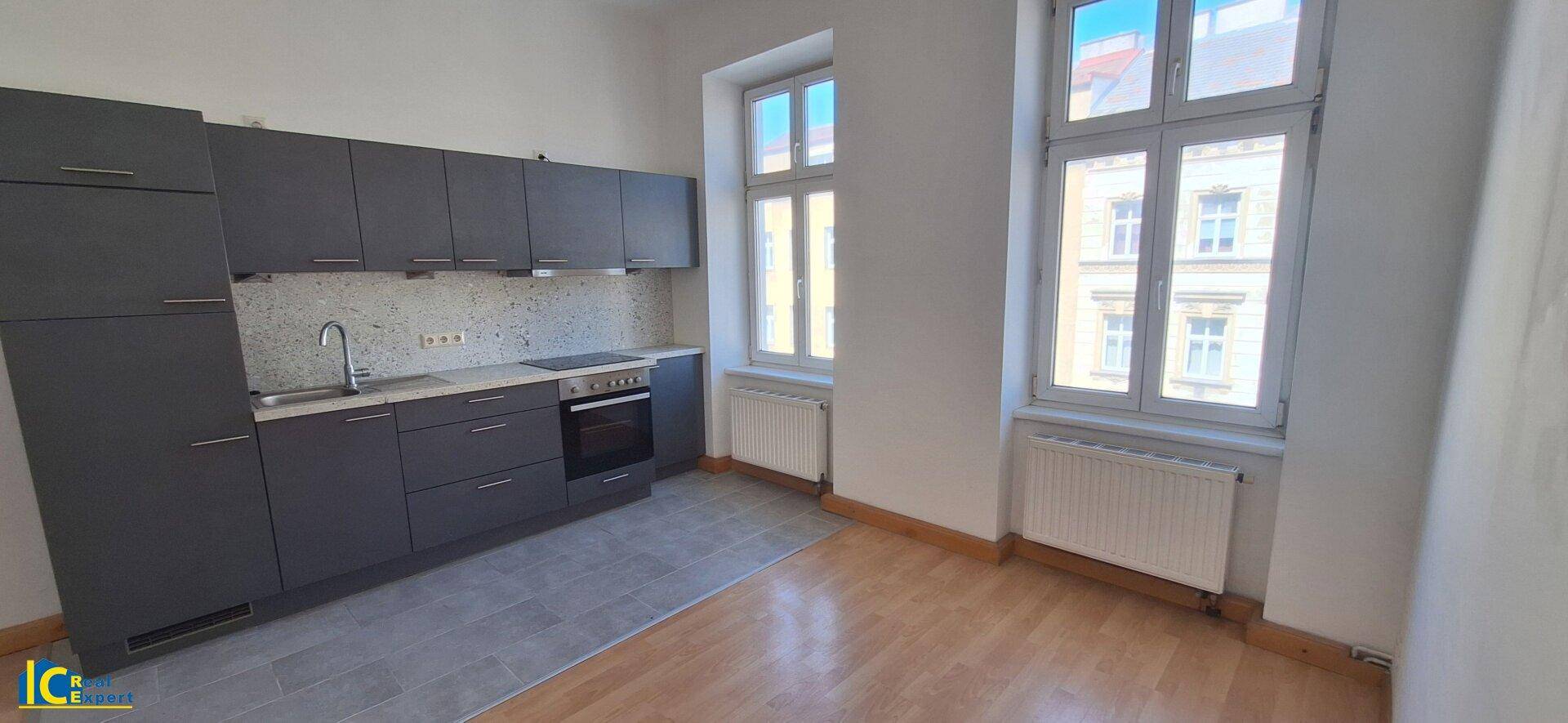 Moderne Küche mit dunkelgrauen Schränken, integrierten Geräten und Fliesenboden im Kochbereich.
