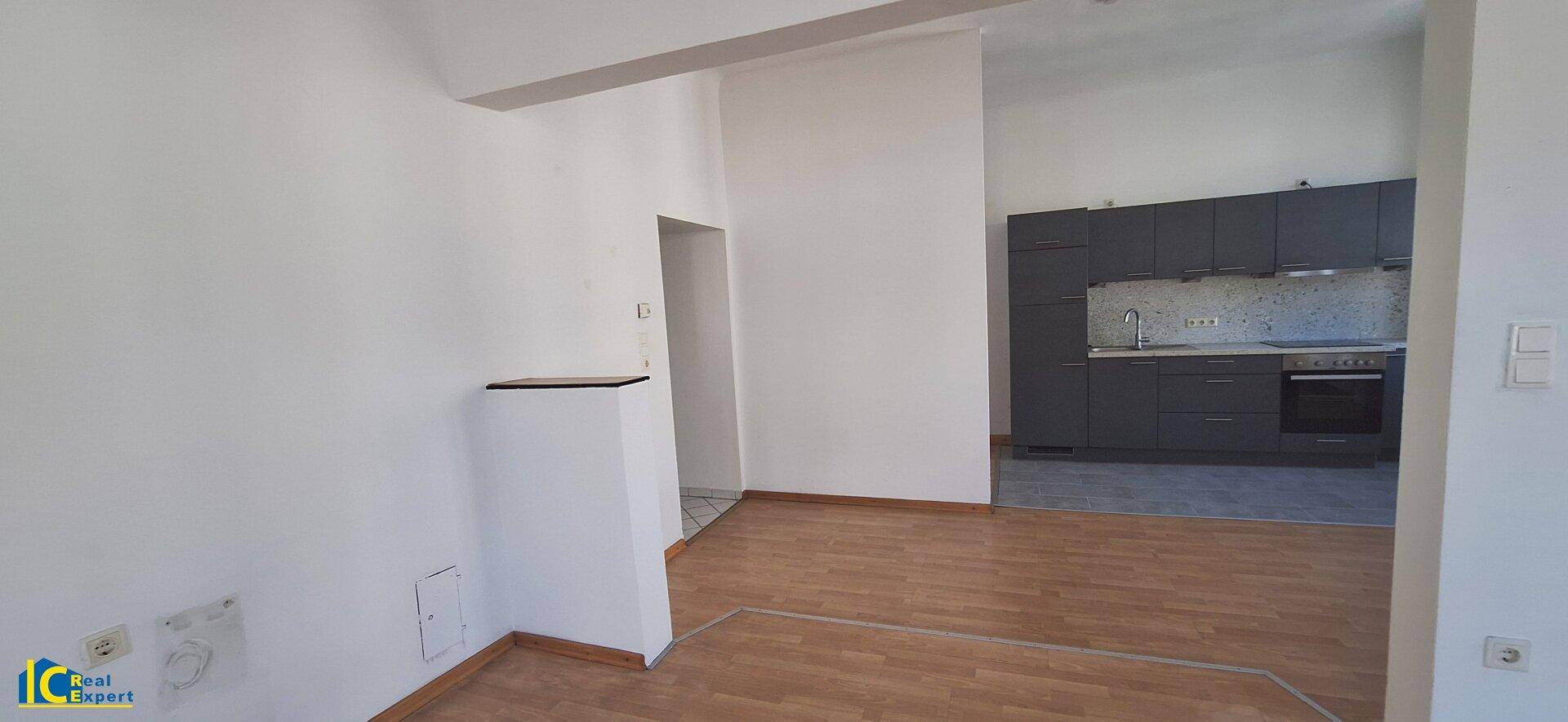 Geräumiger Wohnbereich mit Übergang zur Küche, gekennzeichnet durch unterschiedliche Bodenbeläge.