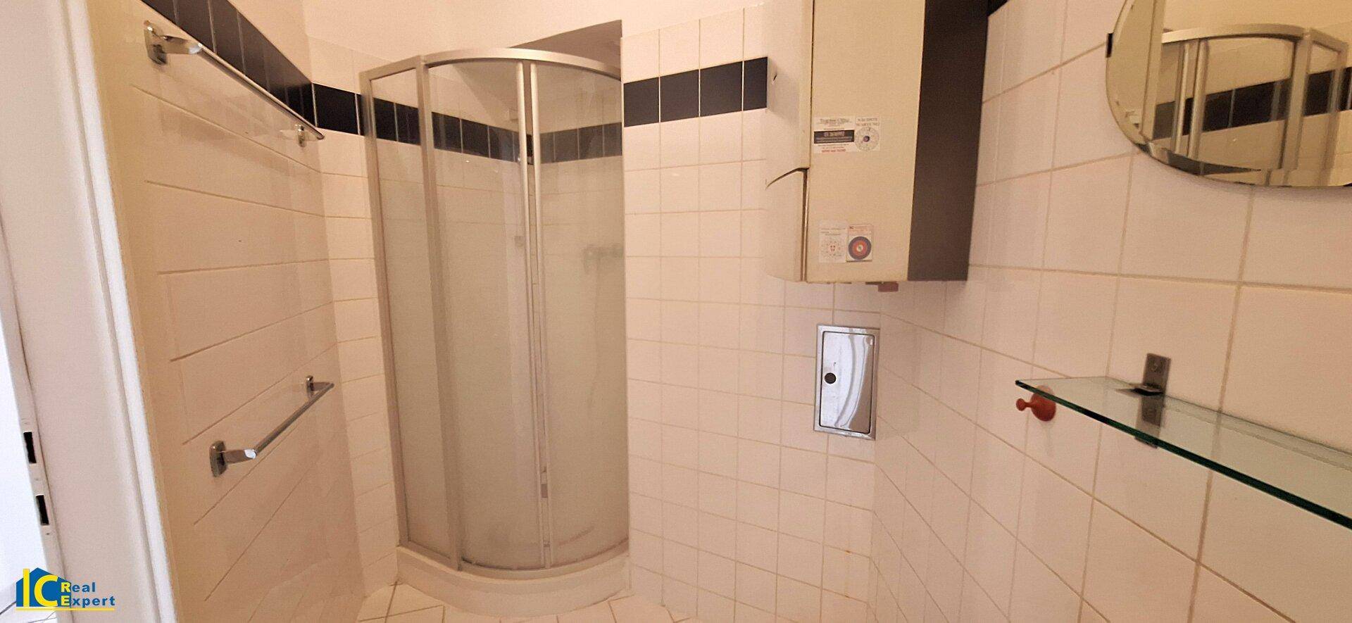 Badezimmer mit Duschkabine, weißen Fliesen und einem Warmwasserboiler an der Wand.