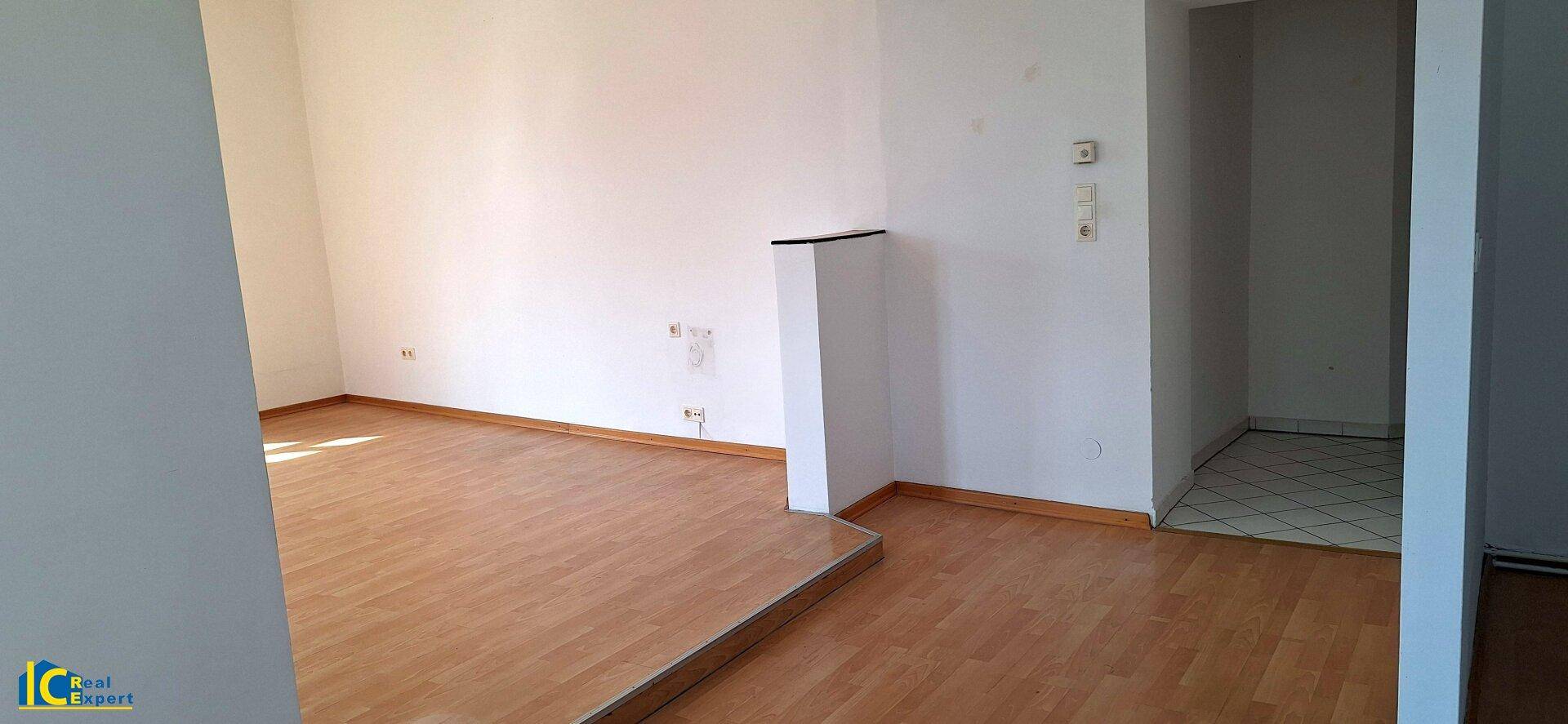 Heller Wohnbereich mit Holzfußboden und Zugang zu einem weiteren Raum, gut erhalten.