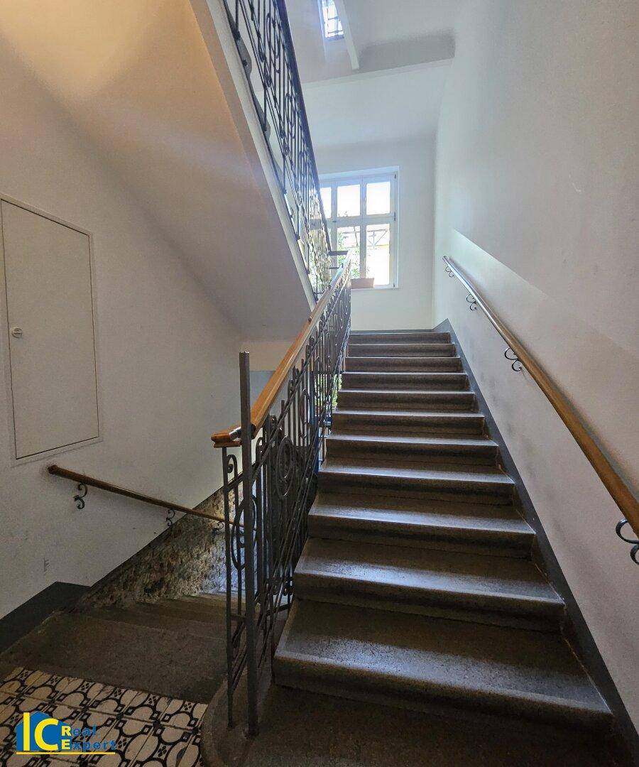 Historisches Treppenhaus mit schmiedeeisernem Geländer und natürlichem Lichteinfall durch ein Fenster.