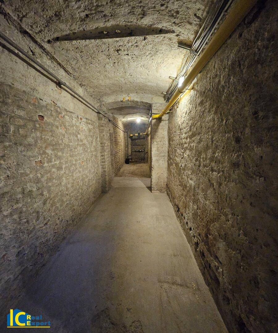 Langer, gewölbter Kellergang mit unverputzten Ziegelwänden und Betonboden, gut beleuchtet und funktional.