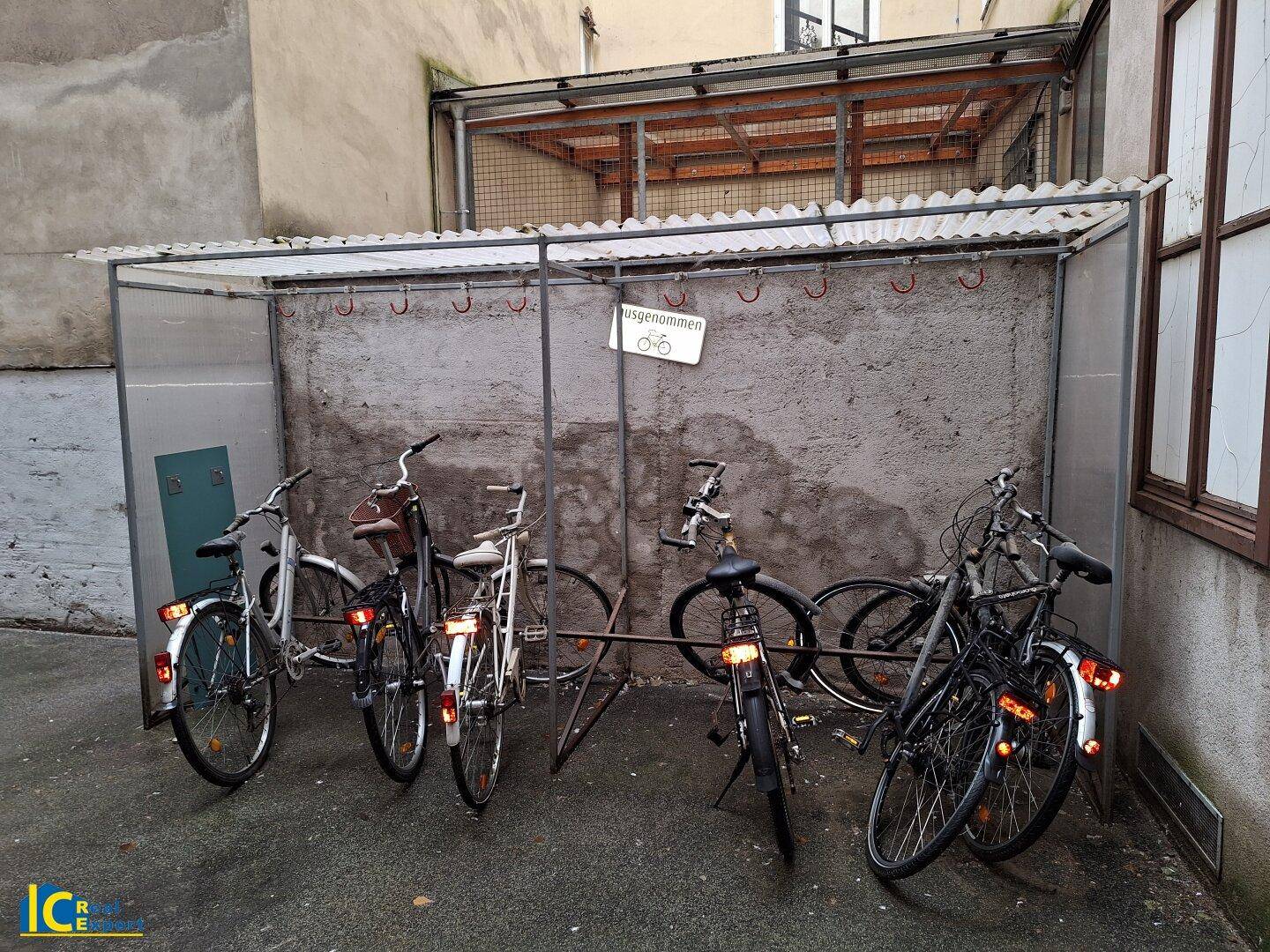 Überdachter Fahrradabstellplatz mit mehreren Fahrrädern an einer Betonwand.