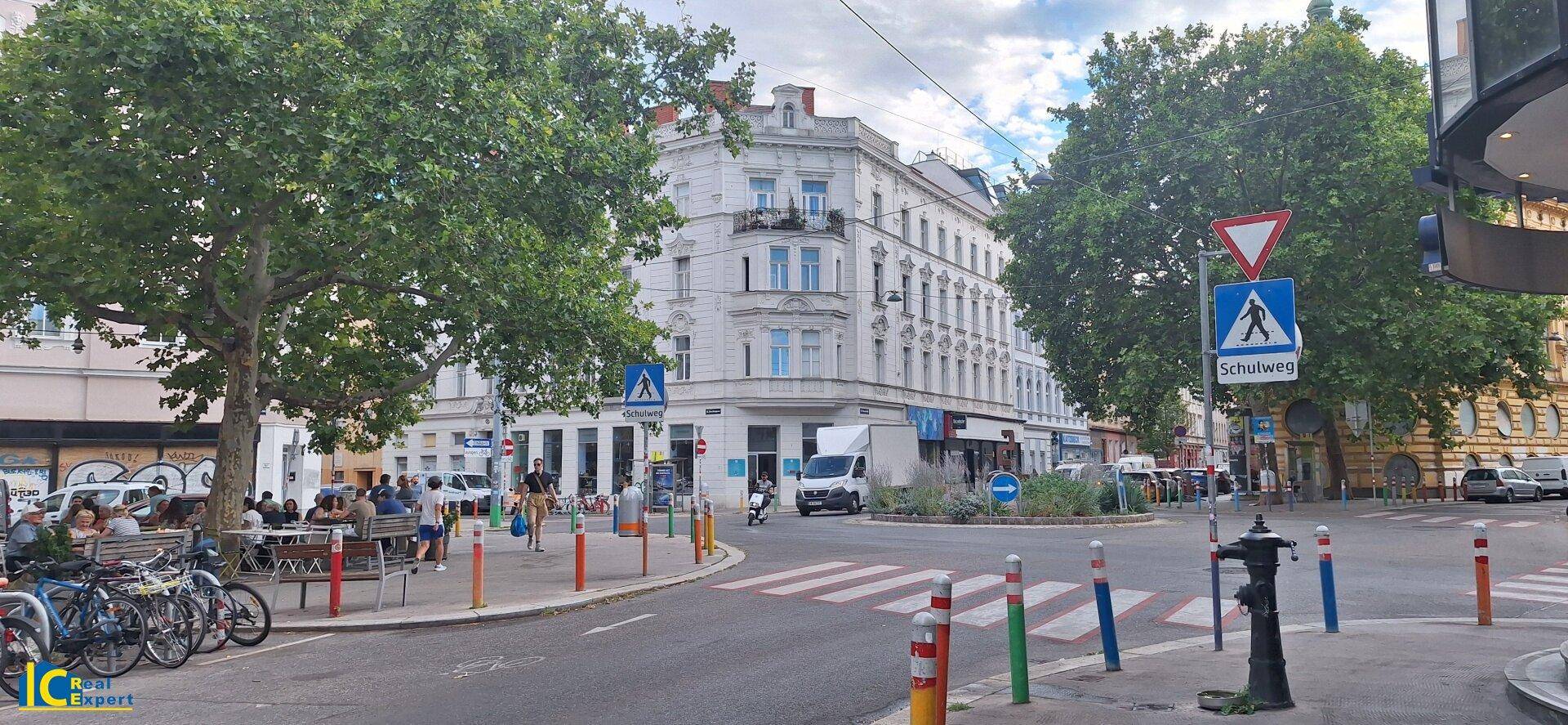 Belebte Straßenkreuzung mit historischen Gebäuden, Bäumen und Fußgängerüberwegen in der Stadt.
