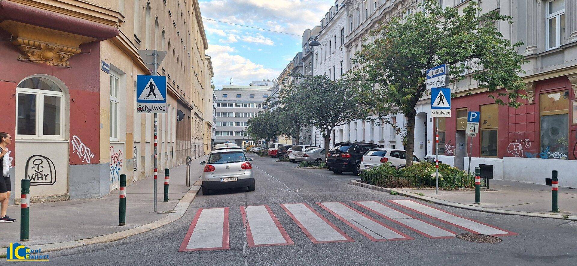 Ruhige Stadtstraße mit Zebrastreifen, parkenden Autos und historischen Gebäuden im Hintergrund.