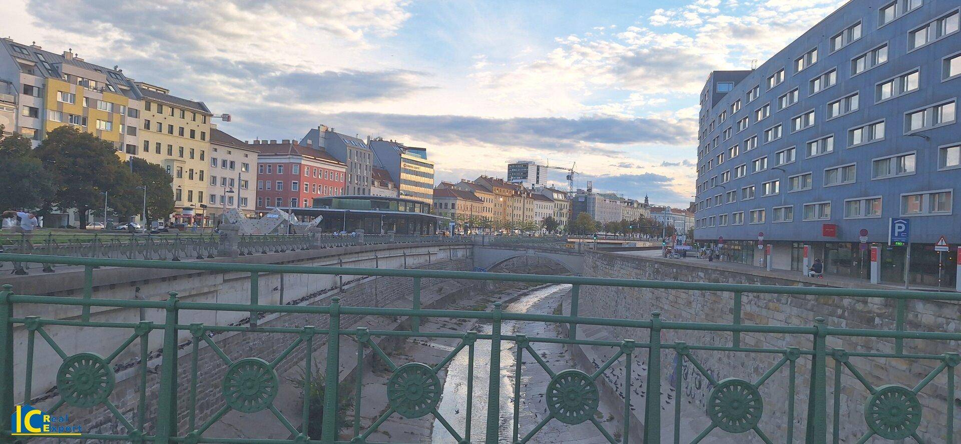 Blick über einen Kanal mit grüner Brüstung und städtischer Bebauung im Hintergrund unter weitem Himmel.