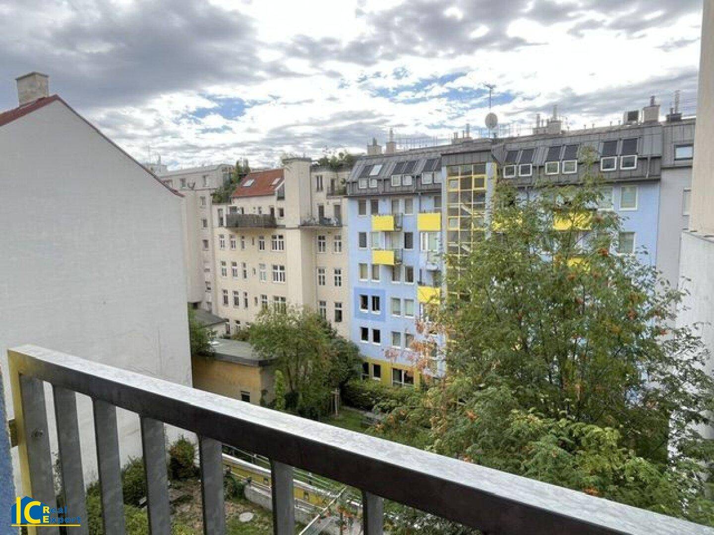 Blick vom Balkon auf die umliegenden Gebäude und grüne Bäume in der Nachbarschaft.