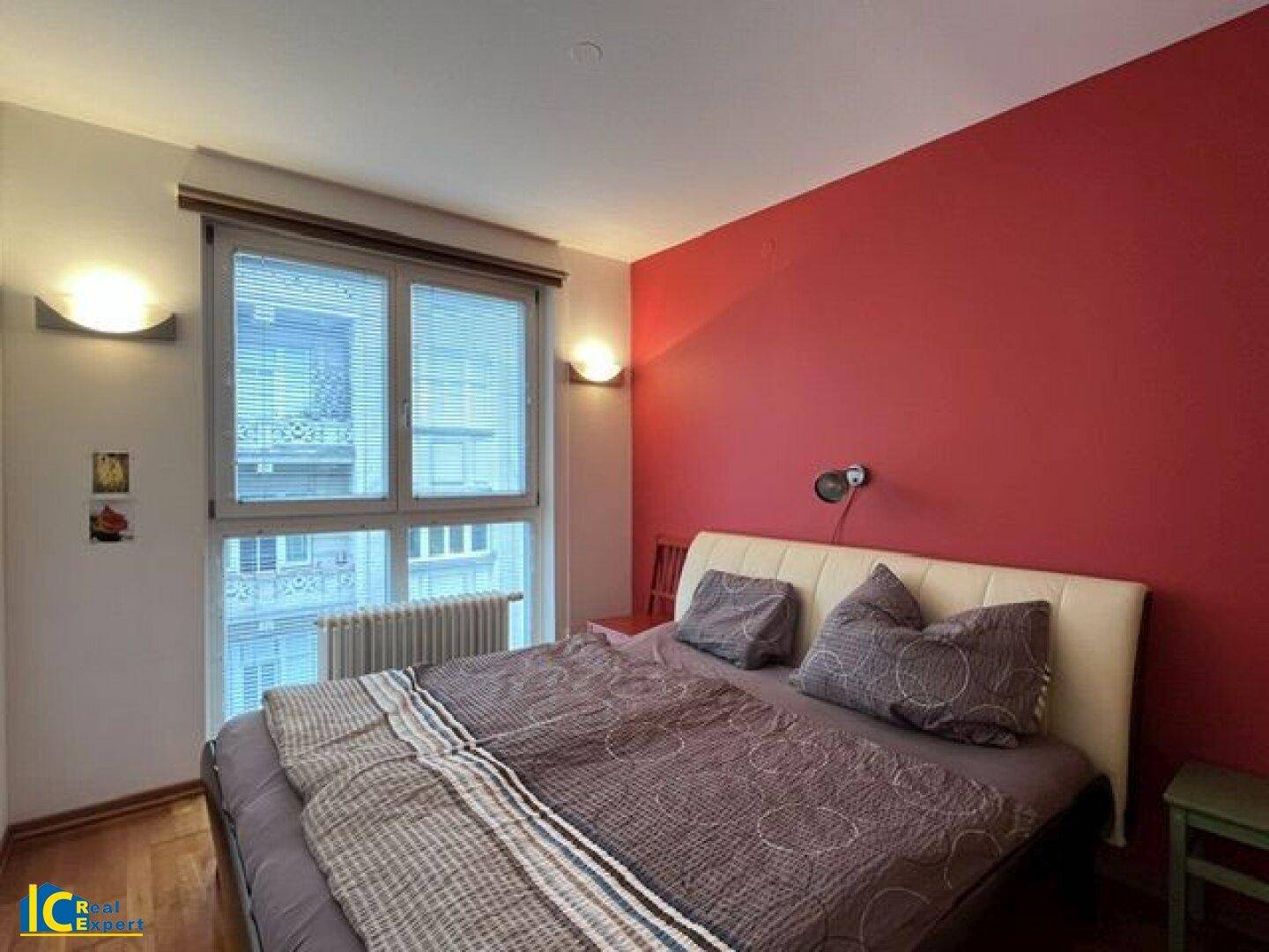 Schlafzimmer mit roter Akzentwand, Doppelbett und großem Fenster mit Blick nach draußen.
