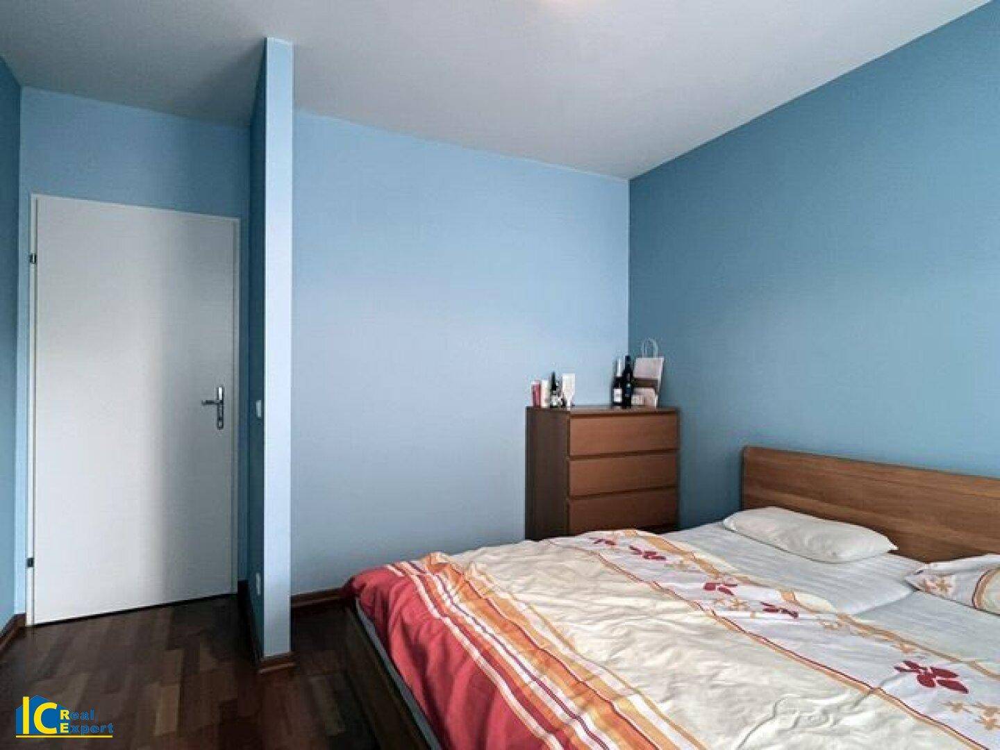 Schlafzimmer mit blauen Wänden, Holzbett und Tür, die zu einem anderen Raum führt.