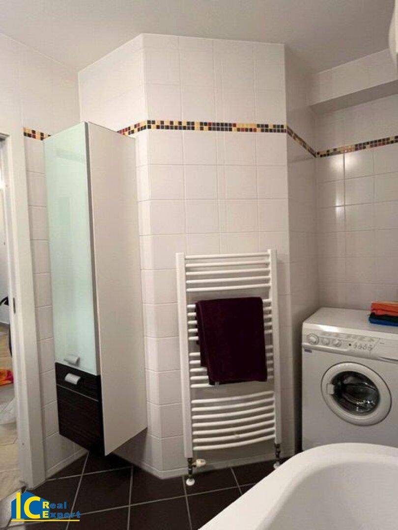 Badezimmer mit Waschmaschine, Handtuchheizkörper und weiß gefliesten Wänden.