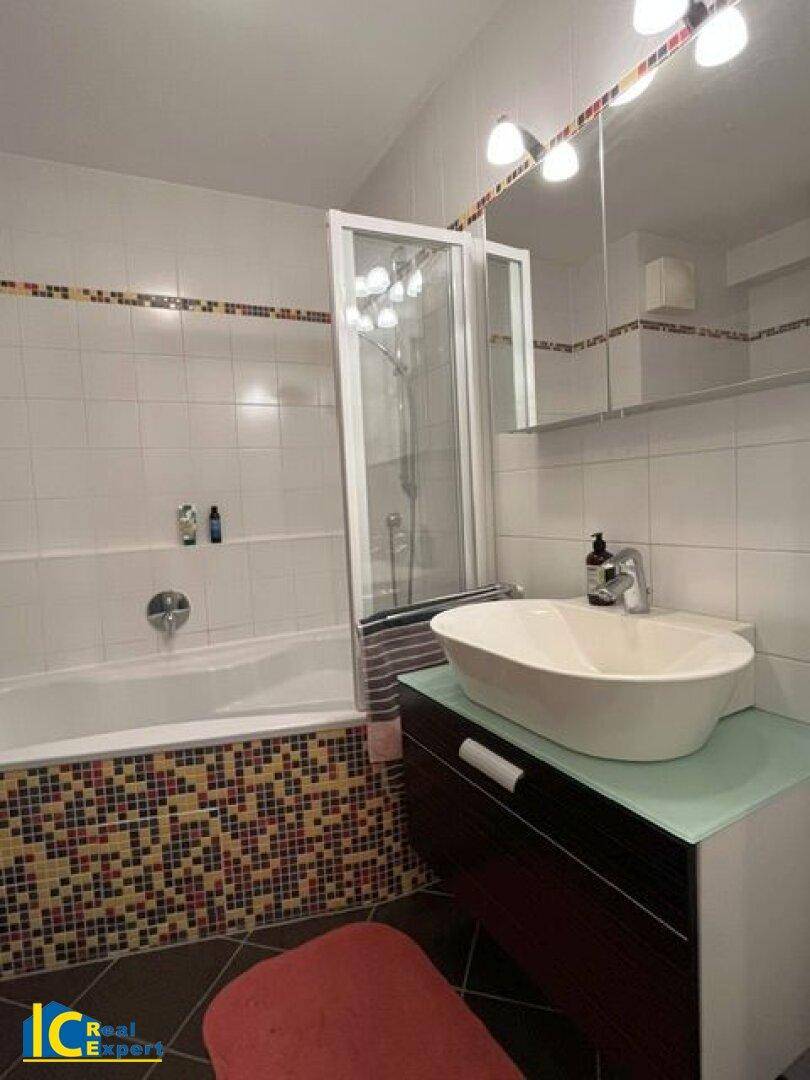 Badezimmer mit Badewanne, Duschabtrennung und Aufsatzwaschbecken auf dunklem Unterschrank.