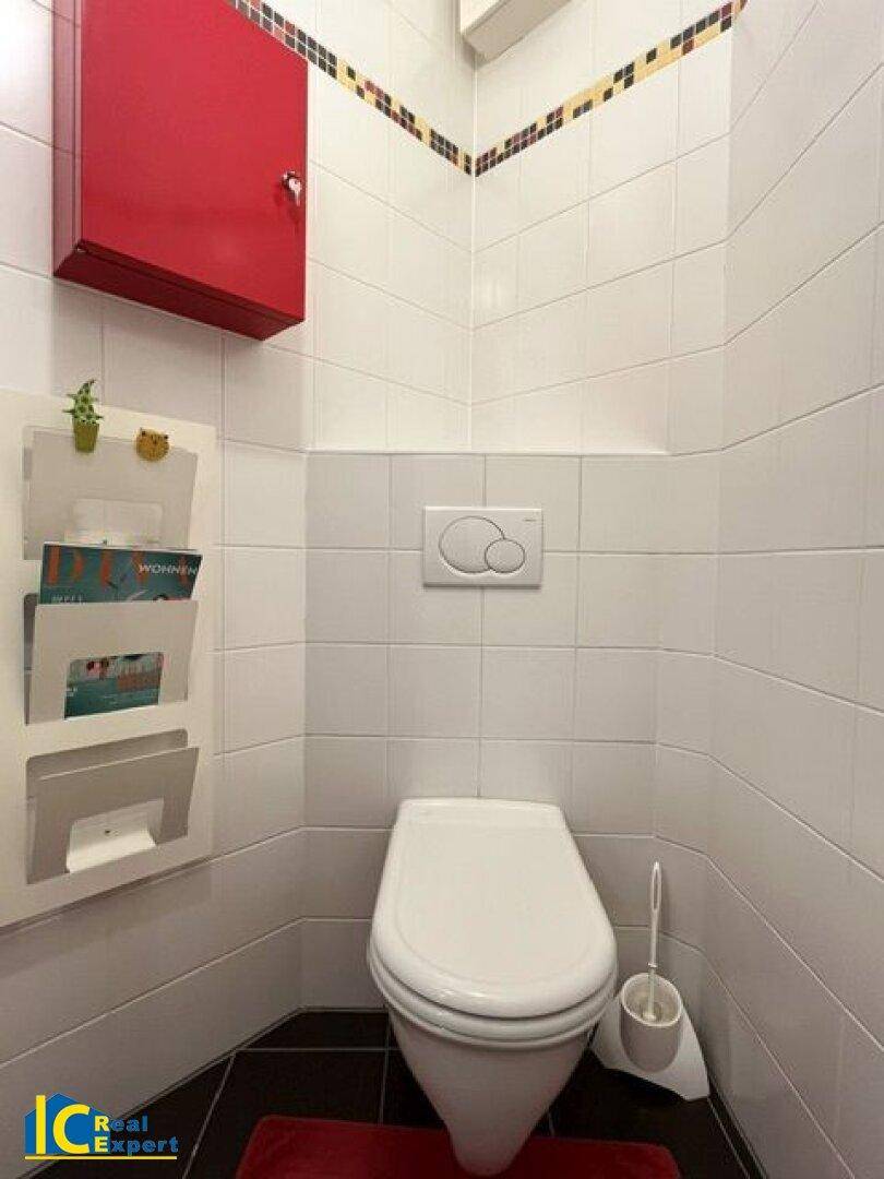 Separates WC mit wandhängender Toilette, weißen Fliesen und rotem Wandschrank.