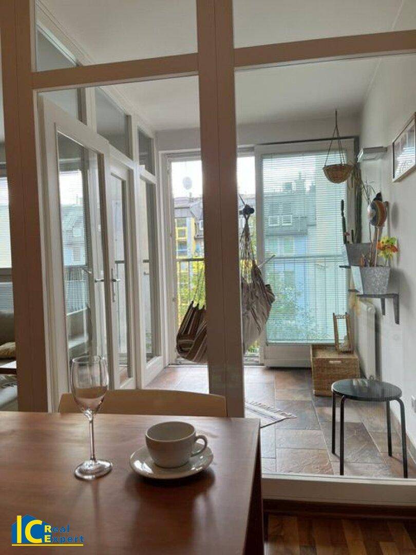 Essbereich mit Holztisch und Blick auf den verglasten Balkon, der zusätzlichen Raum bietet.