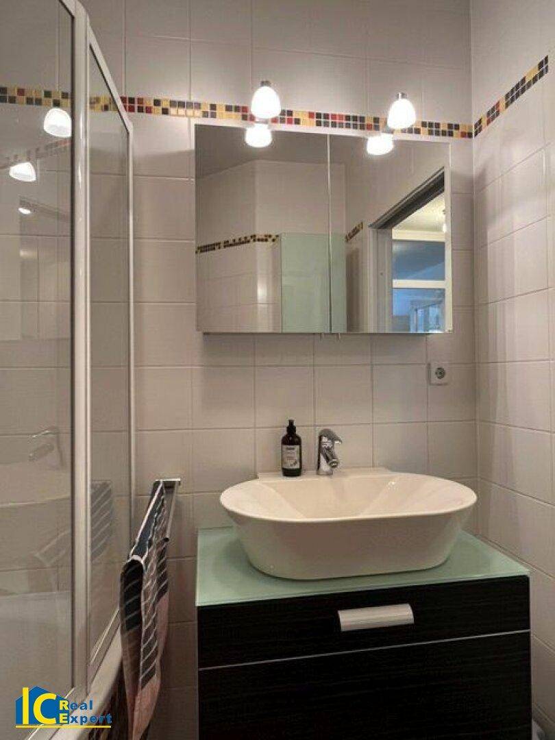Modernes Badezimmer mit Aufsatzwaschbecken, Spiegelschrank und weißen Fliesen.