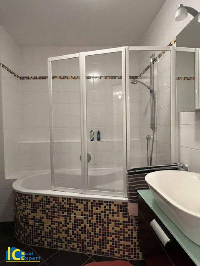 Badezimmer mit Badewanne, Duschabtrennung und farbigen Mosaikfliesen am Wannenrand.