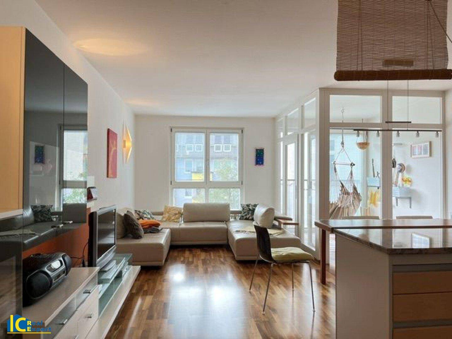 Geräumiger Wohn- und Essbereich mit offener Küche, Holzboden und Zugang zum Balkon.
