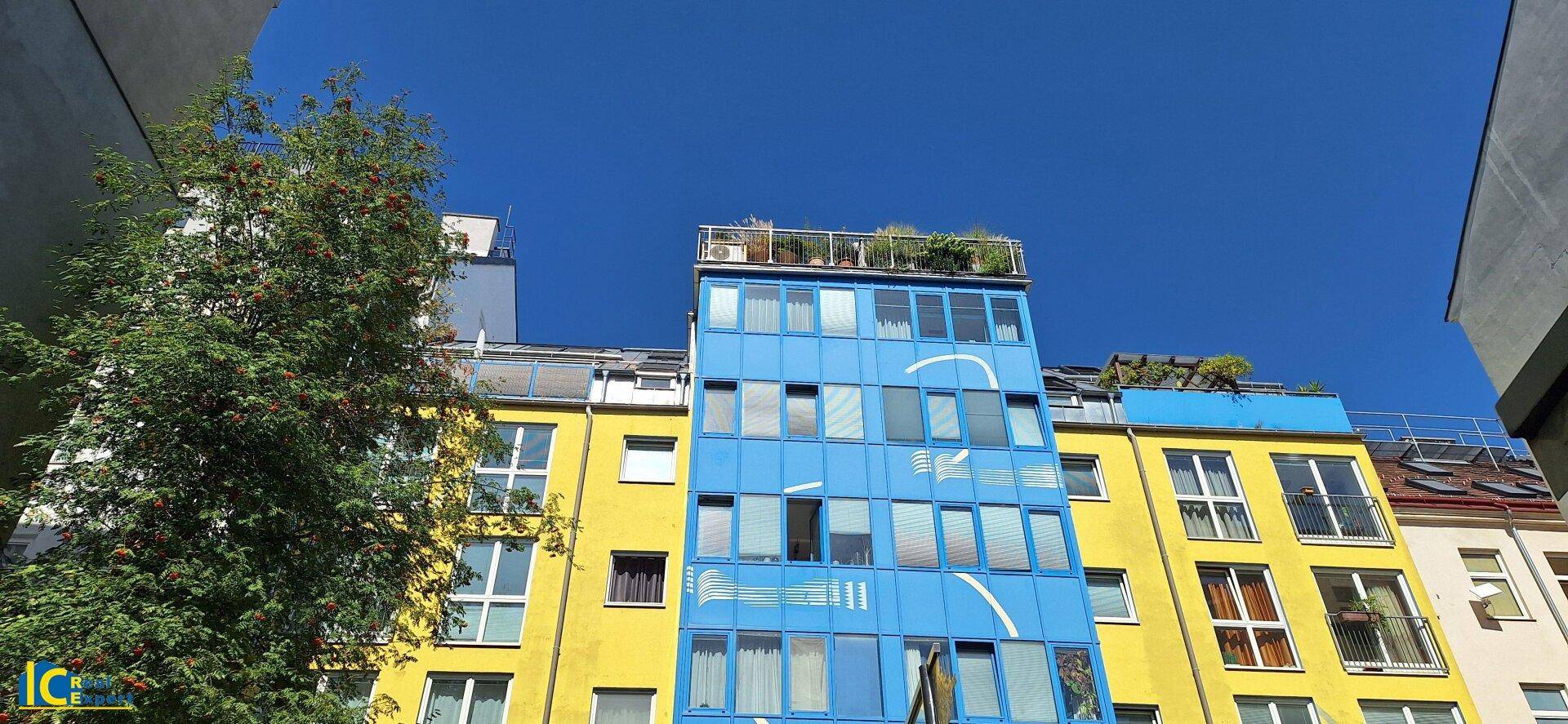 Bunte Fassade eines modernen Gebäudes mit gelben und blauen Elementen sowie einer Dachterrasse.