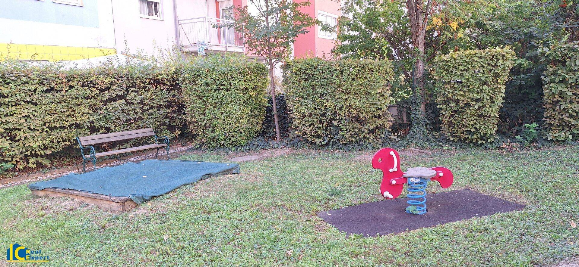 Spielbereich im Gemeinschaftsgarten mit Sandkasten und Federwippe für Kinder.
