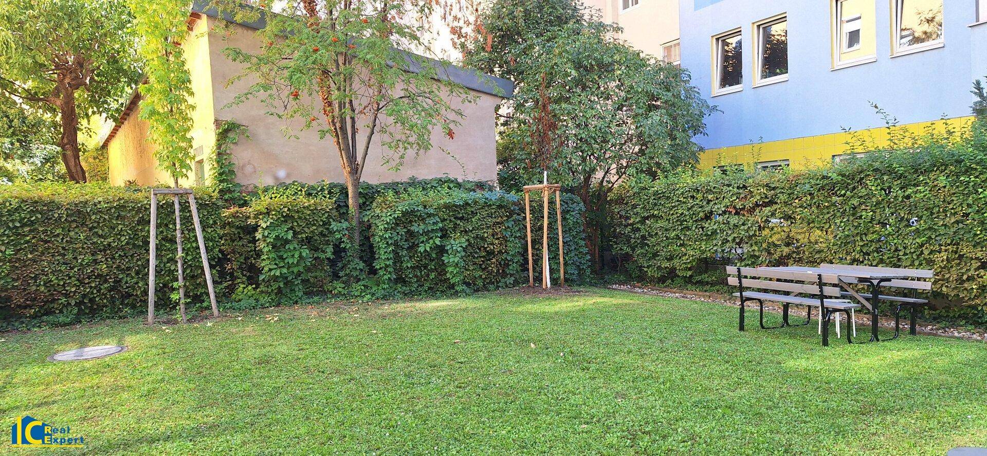 Gepflegter Gemeinschaftsgarten mit Rasenfläche, Hecken und einem Picknicktisch für entspannte Stunden.