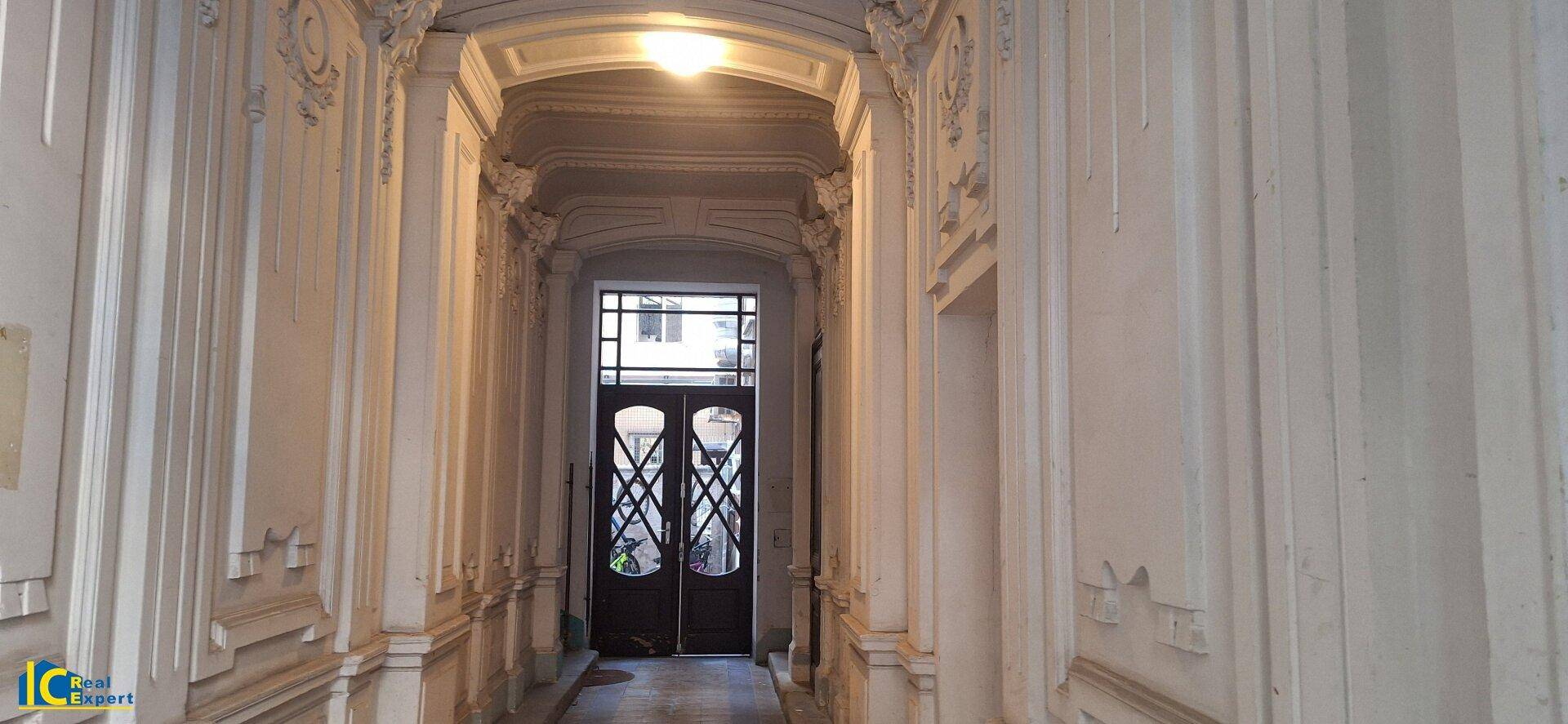 Historischer Flur mit aufwendigen Stuckverzierungen an den Wänden und einer verzierten Eingangstür am Ende.