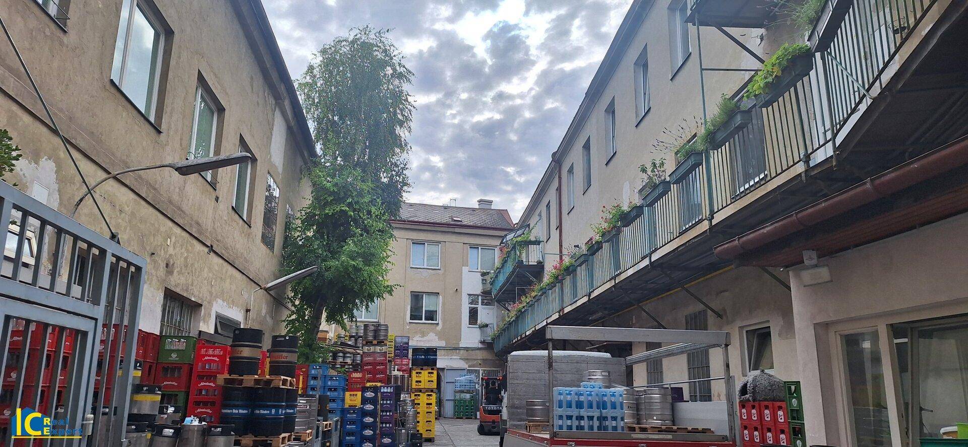 Hinterhof zwischen älteren Gebäuden mit gestapelten Kisten, einem Baum und Balkonen an der Fassade.