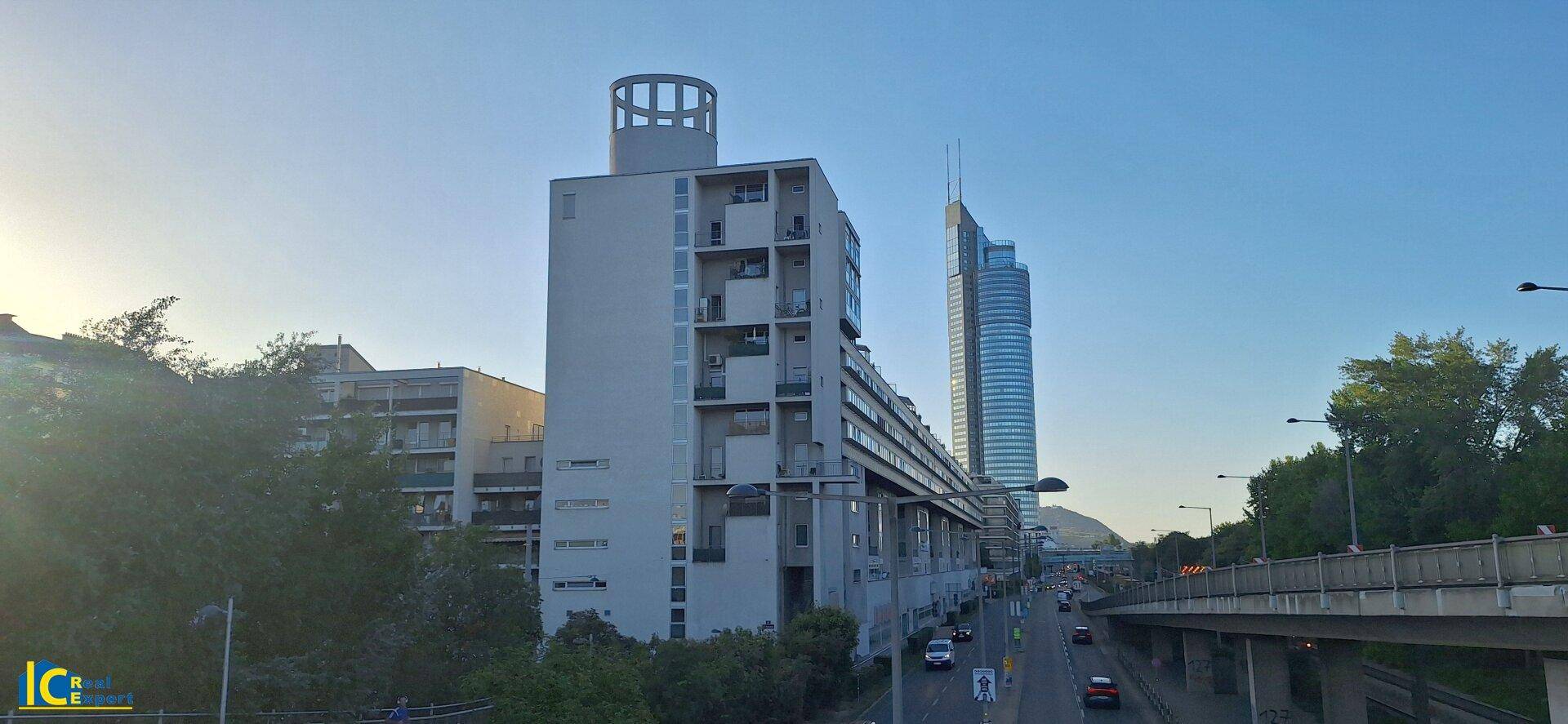 Städtische Ansicht mit modernen Gebäuden, einer belebten Straße und einer Brücke unter blauem Himmel.