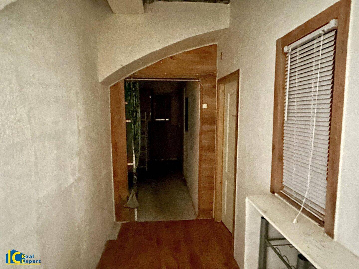 Schmaler Flur mit Holzboden und einem Fenster, das natürliches Licht hereinlässt.