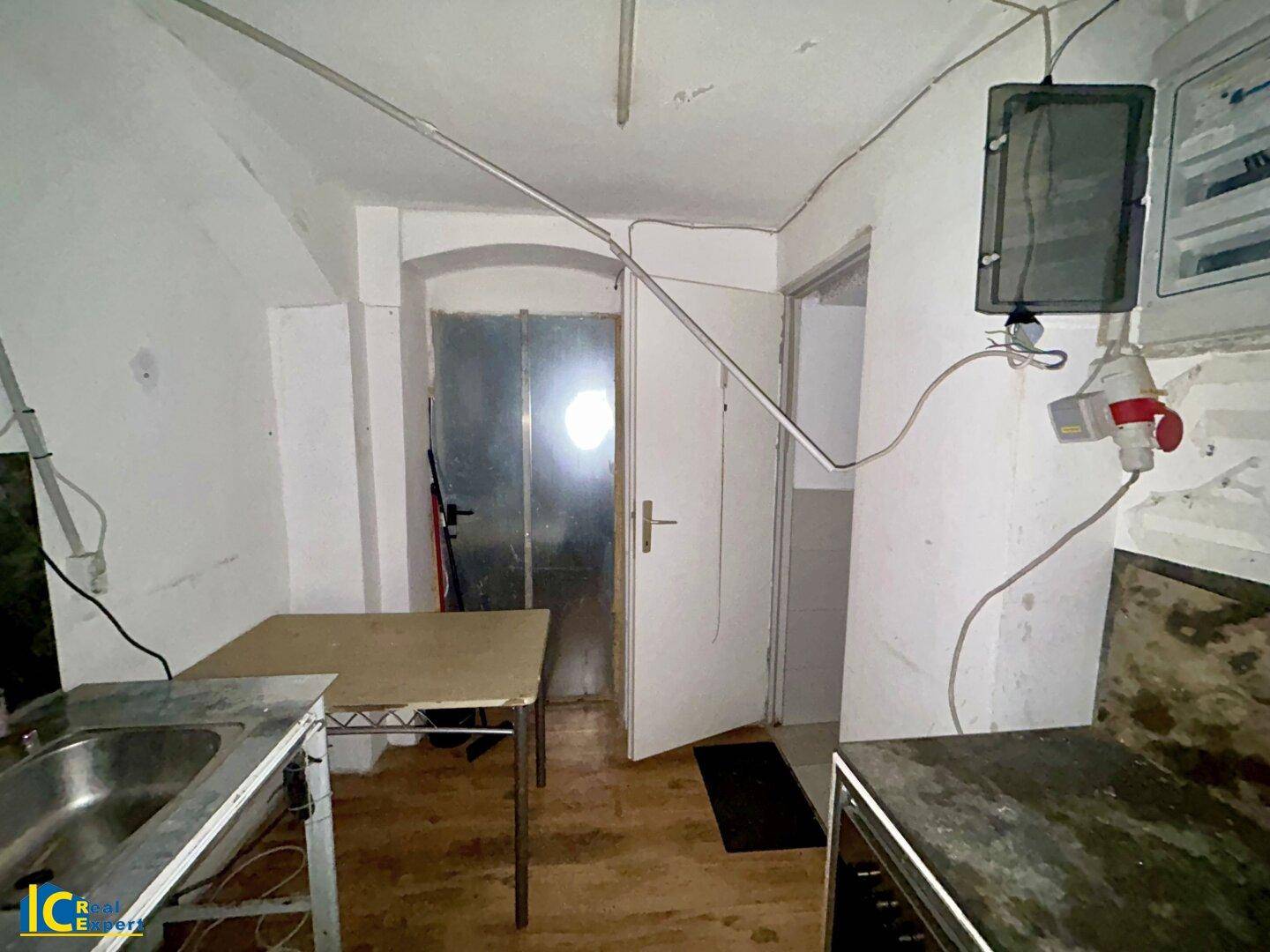 Kellerraum mit Spüle, Tisch und verschiedenen Installationen, funktional eingerichtet.