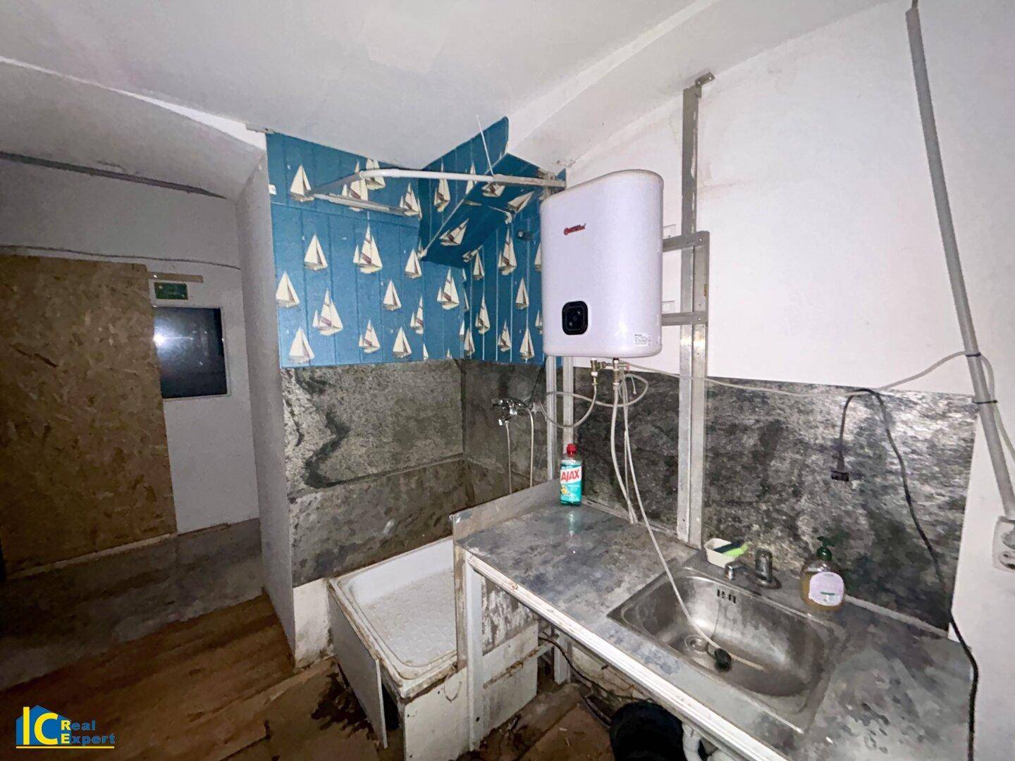Kellerraum mit Waschbecken, Boiler und provisorischer Duschlösung.