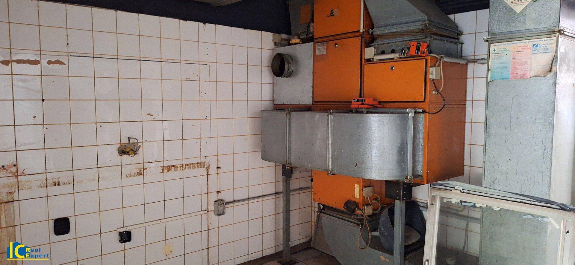 Technikraum mit großen orangefarbenen Lüftungsanlagen und gefliesten Wänden in renovierungsbedürftigem Zustand.