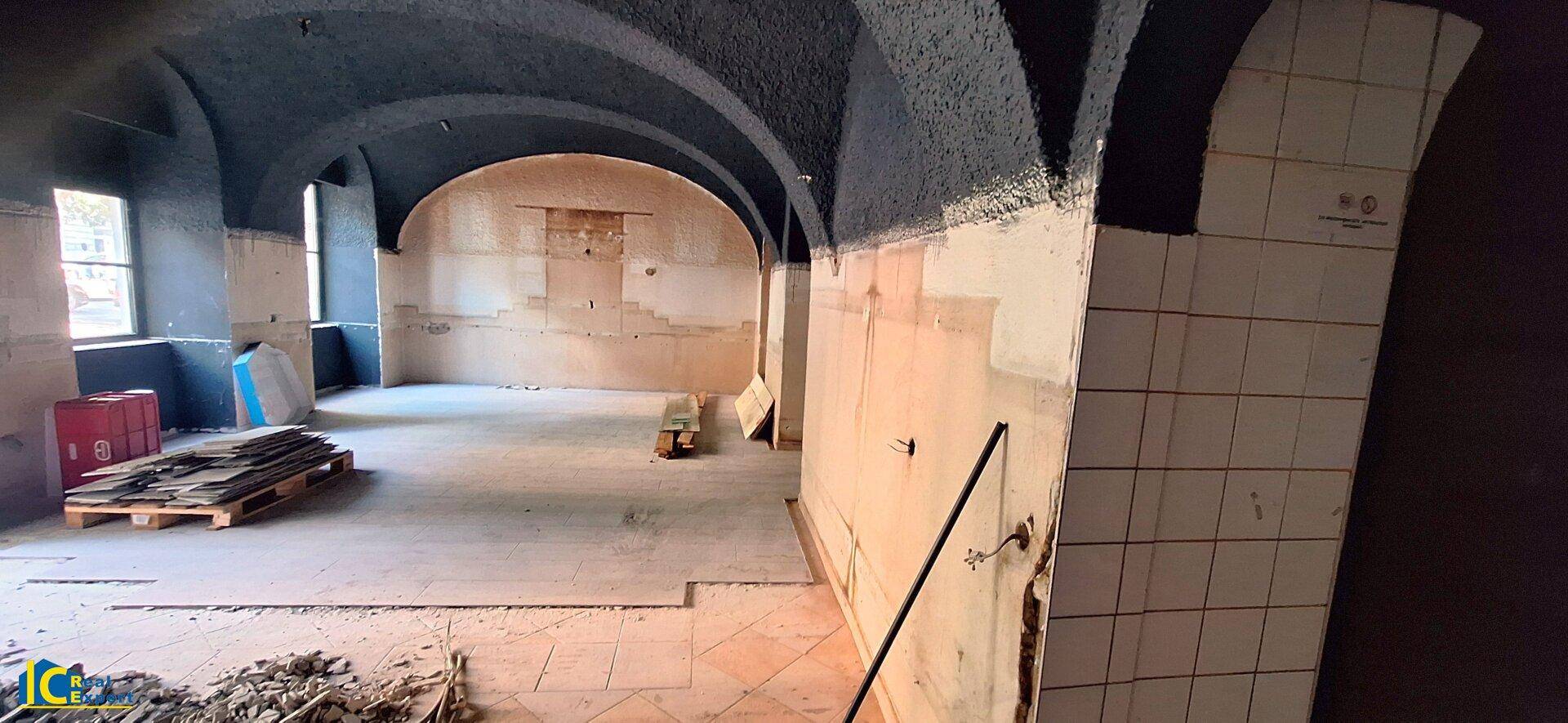 Geräumiger Kellerraum mit hohen Gewölbedecken, großen Fenstern und rohen Wänden, ideal für Umbau.