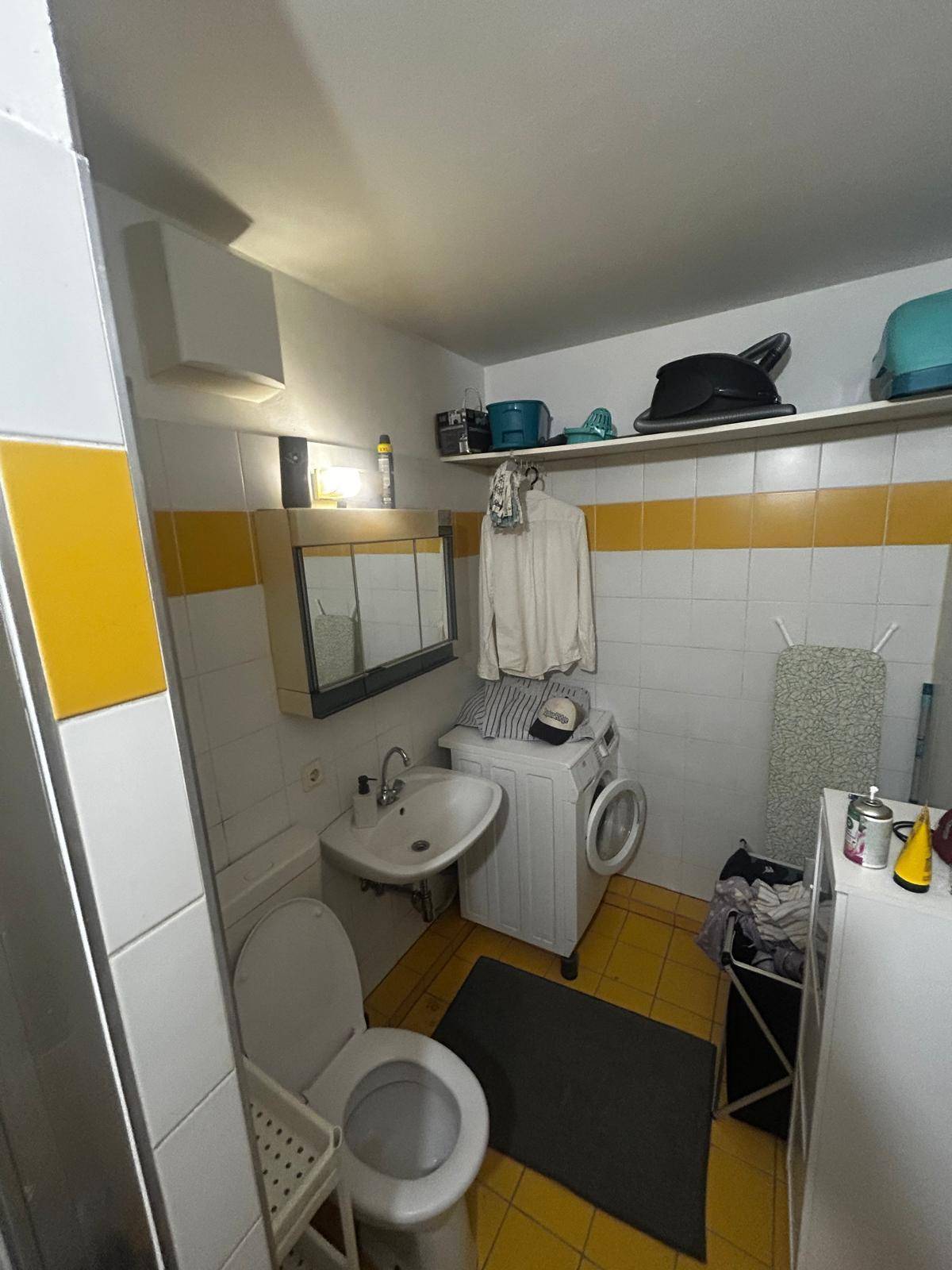 Badezimmer mit WC, Waschbecken und Waschmaschine, ausgestattet mit gelben und weißen Fliesen.