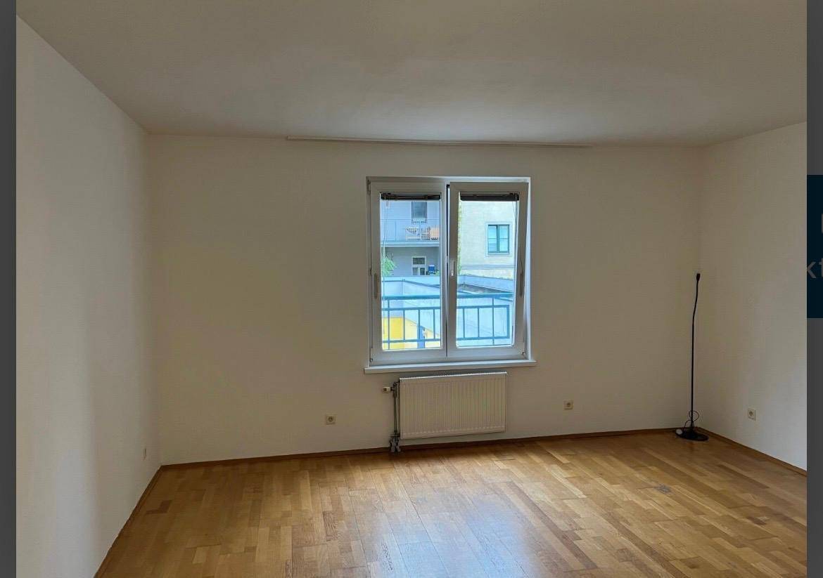 Leeres Wohnzimmer mit Parkettboden und Fenster mit französischem Balkon, bietet viel Tageslicht.