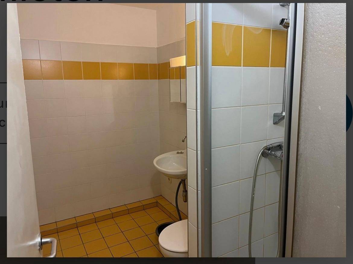 Badezimmer mit Duschkabine, WC und Waschbecken, gefliest in Gelb und Weiß.