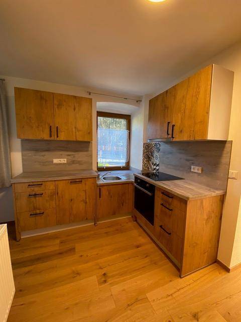Moderne Küche mit Holzschränken, Spüle unter dem Fenster, Induktionskochfeld und Backofen.
