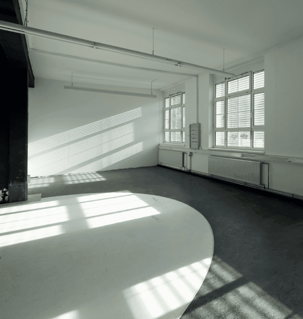 Heller Innenraum mit großen Fenstern und Jalousien, die Streifen von Sonnenlicht auf den Boden werfen.