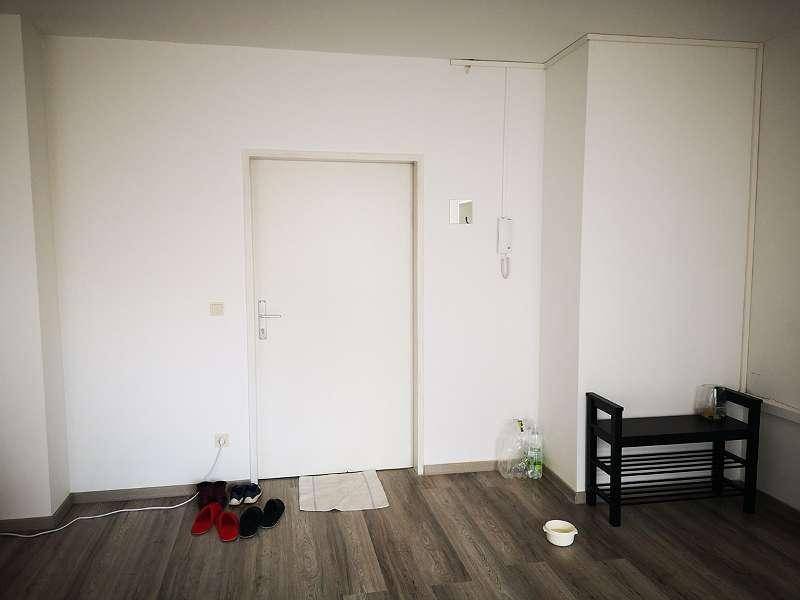 Eingangsbereich mit weißer Tür, Gegensprechanlage und Schuhregal.