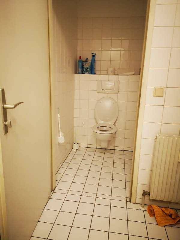 Einfaches Badezimmer mit weißen Fliesen, Toilette und Heizkörper.