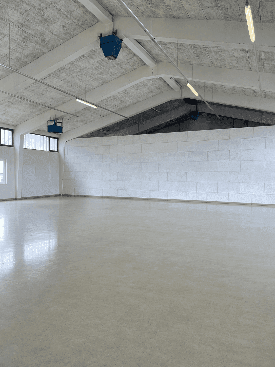 Weitläufige, leere Industriehalle mit hohen Decken, Betonboden und sichtbaren Lüftungseinheiten.