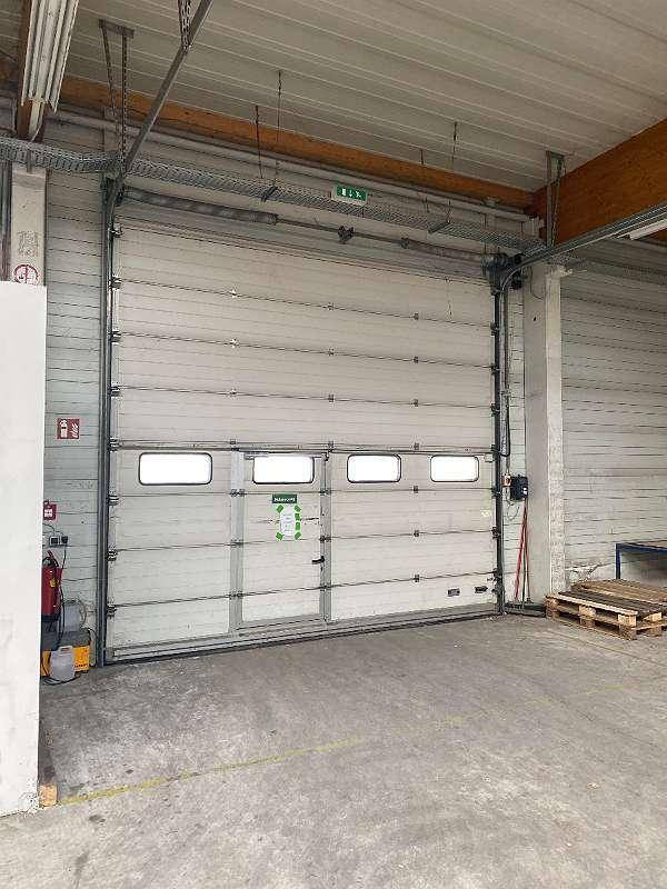 Großes weißes Sektionaltor mit integrierter Zugangstür und kleinen Fenstern in einer Industriehalle.