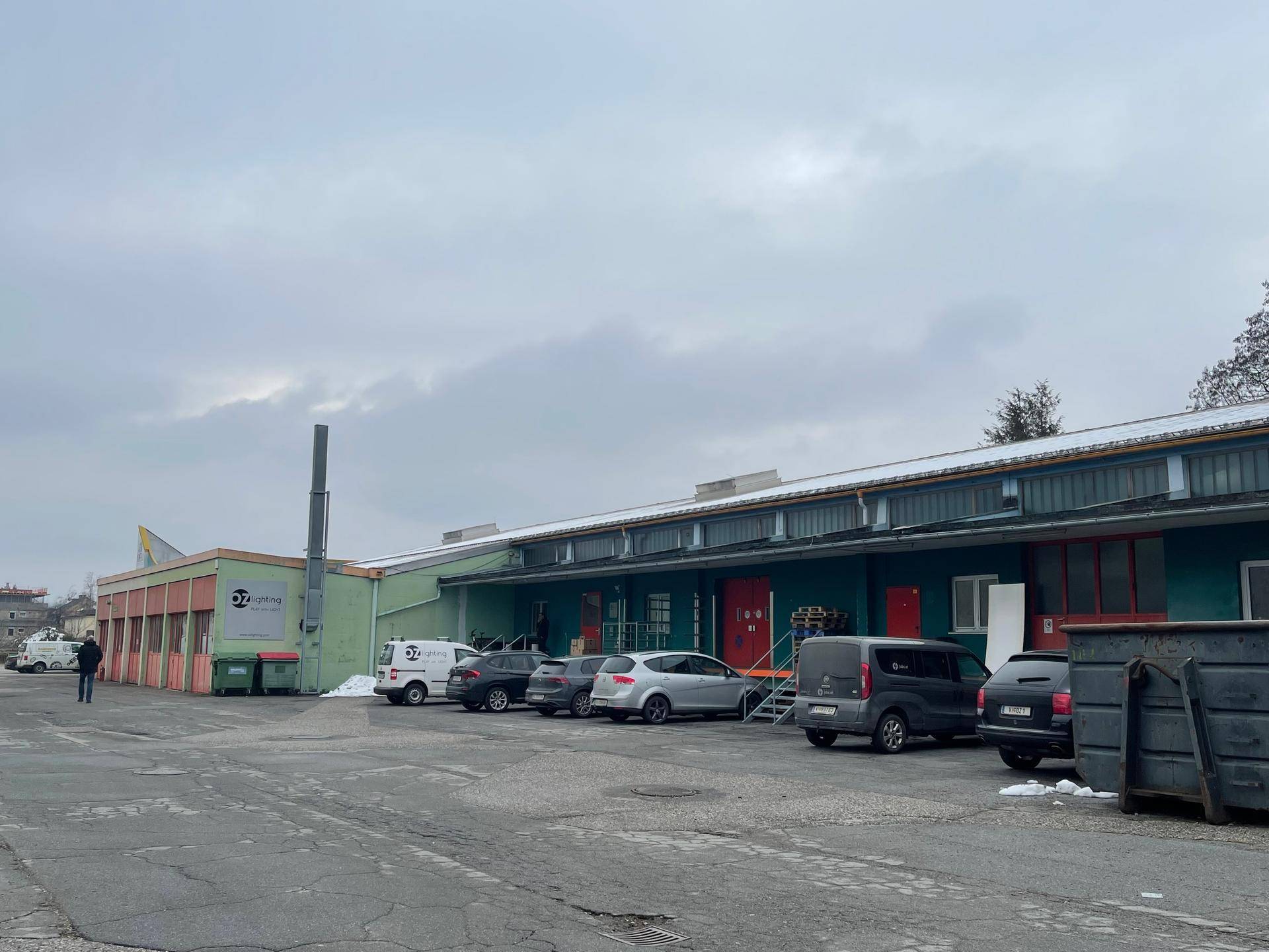 Außenansicht eines Industriegebäudes mit Laderampen, geparkten Fahrzeugen und einem trüben Winterhimmel.