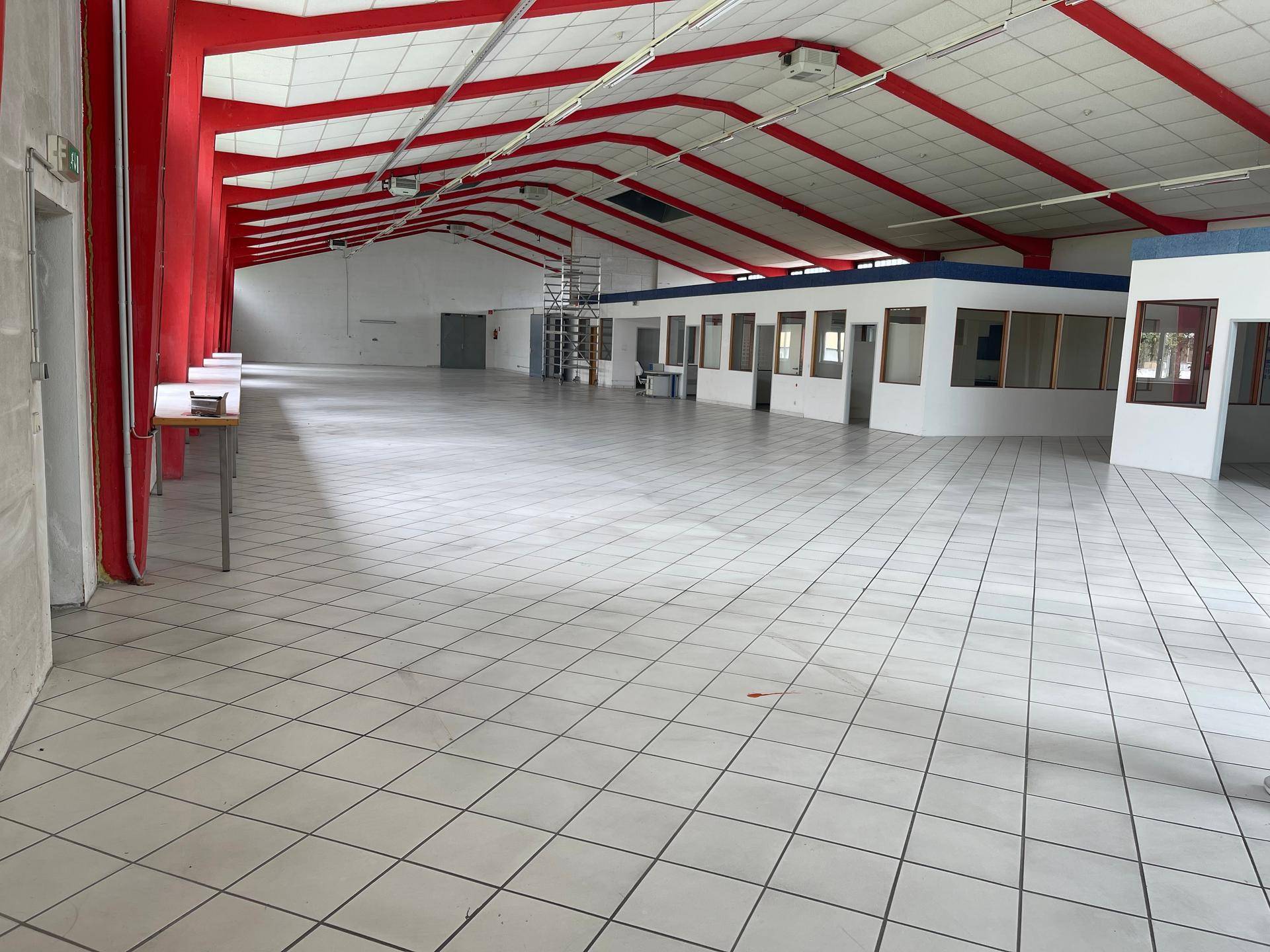 Große, leere Lagerhalle mit weiß gefliestem Boden, hohen Decken und auffälligen roten Trägerstrukturen.