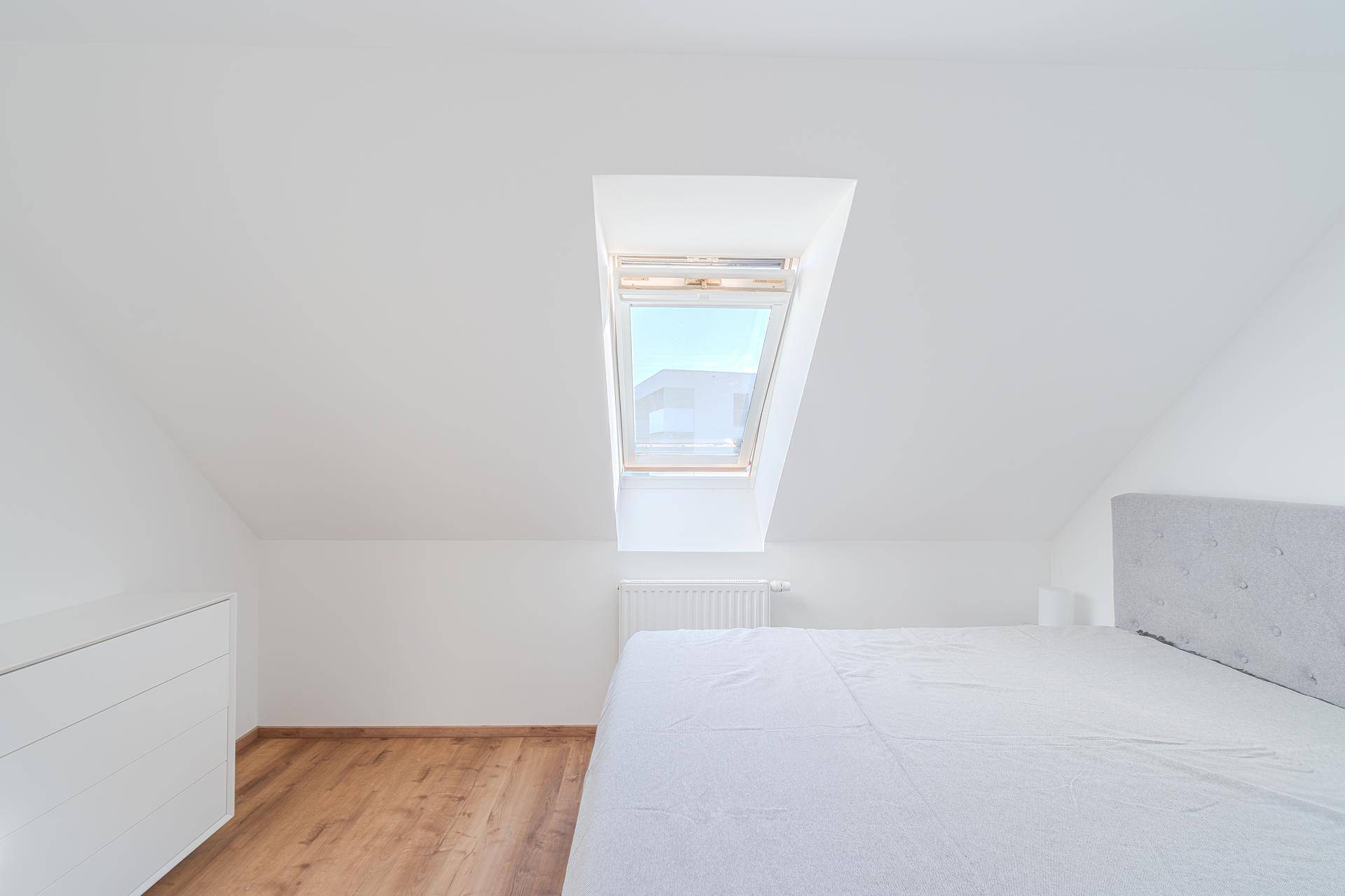 Gemütliches Schlafzimmer im Dachgeschoss mit Holzboden, Bett und einem Dachfenster.