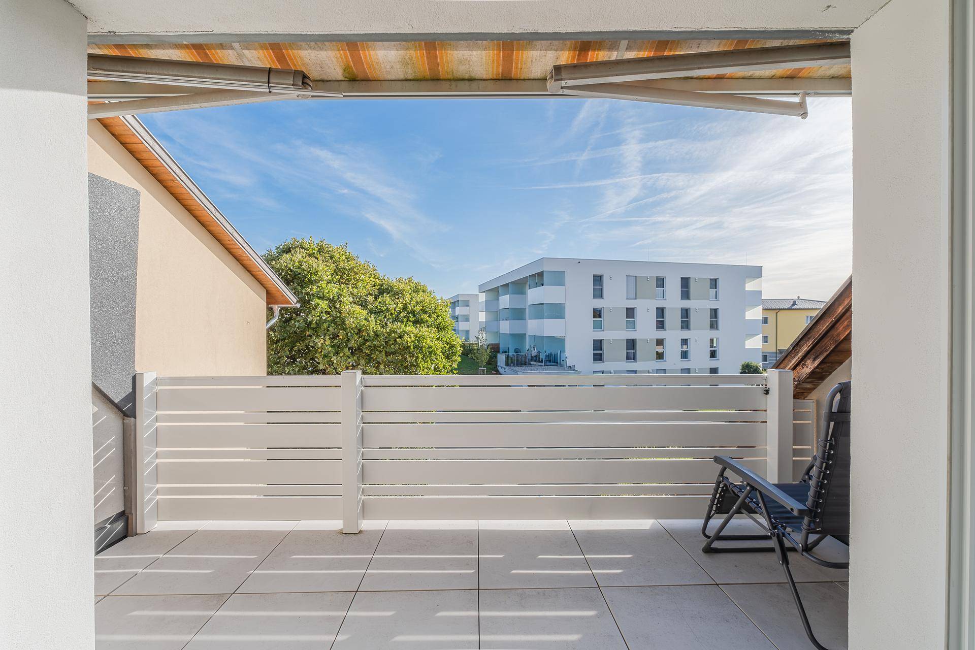 Geräumiger Balkon mit Fliesenboden, Liegestuhl und Blick auf die umliegenden Gebäude.