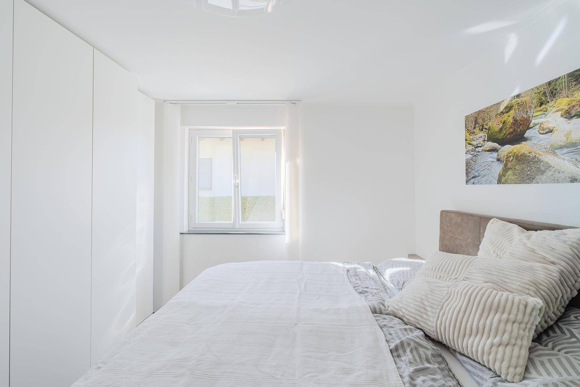 Helles Schlafzimmer mit Doppelbett, weißen Einbauschränken und Fenster.