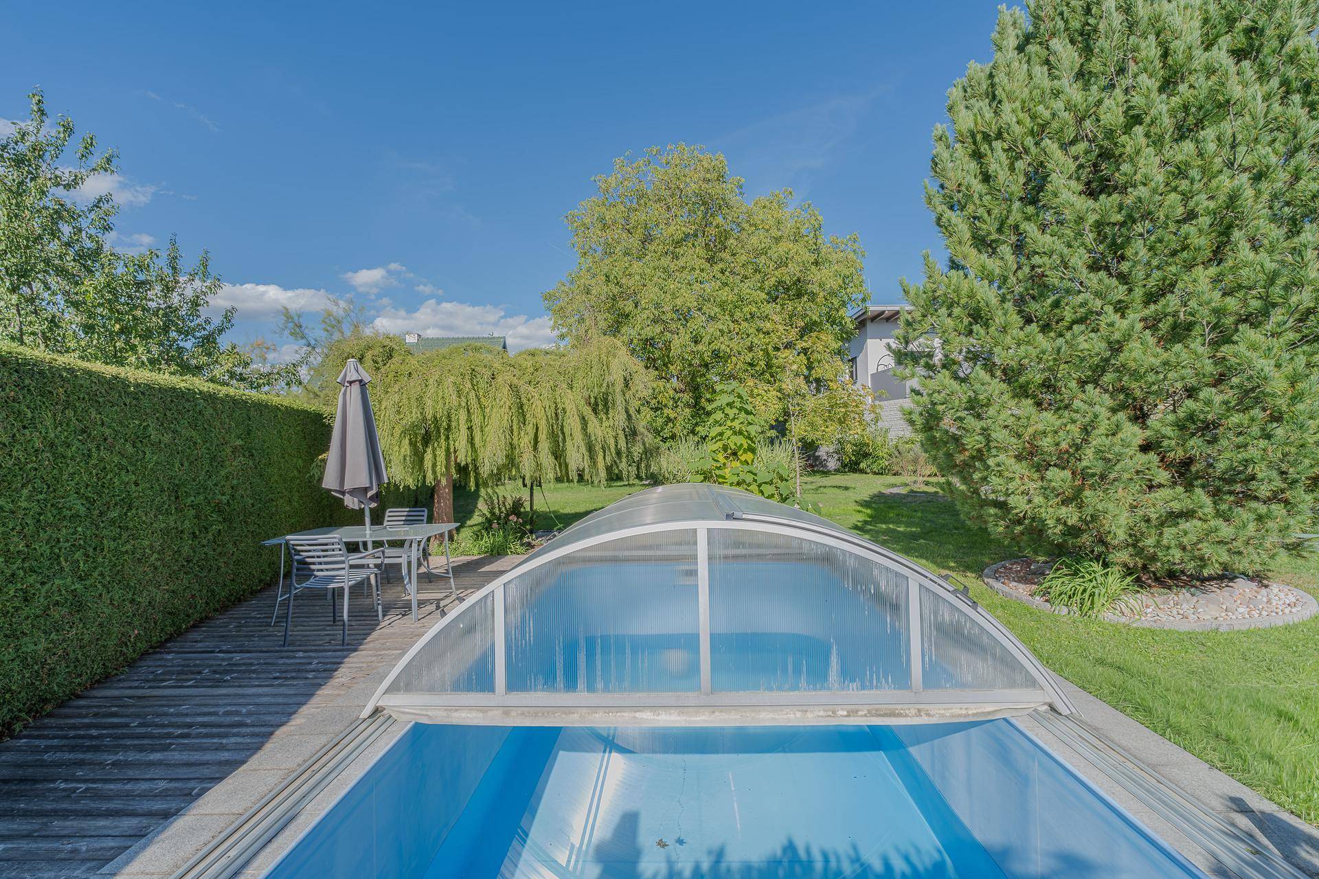 Gepflegter Gartenbereich mit überdachtem Pool, Holzterrasse und Sitzgelegenheiten im Freien.